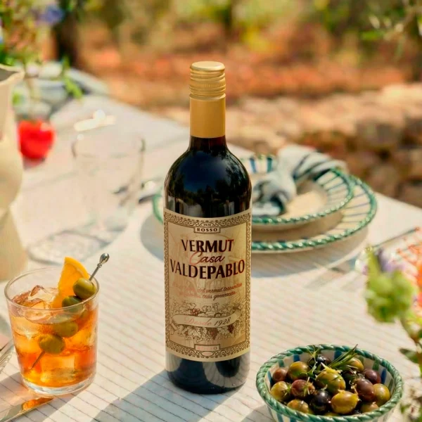 Botella de Vermut Casa Valdepablo con copa de vermut y aceitunas sobre mesa de terraza